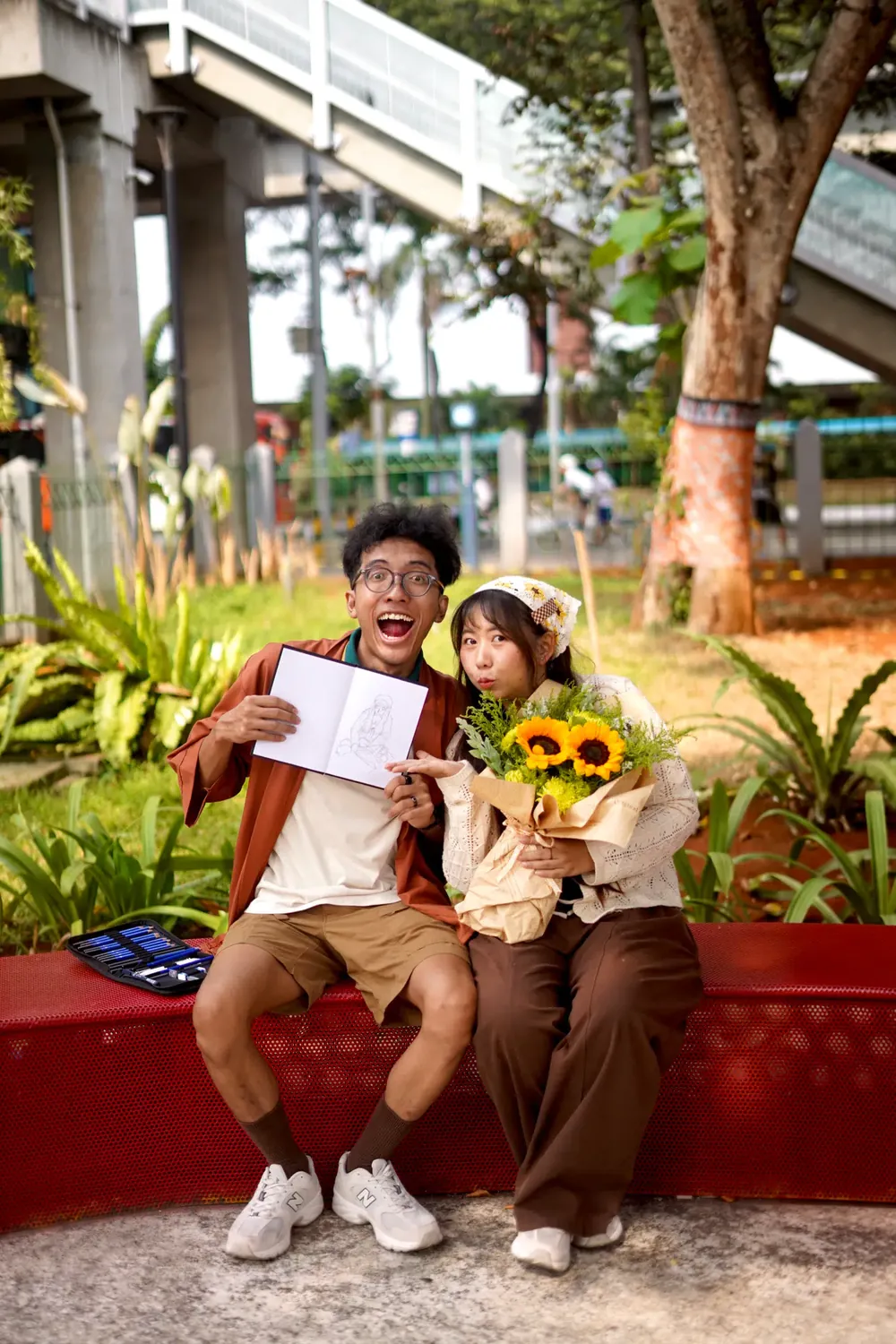 Satria dan Febianti tertawa di bangku taman bersama buket bunga matahari